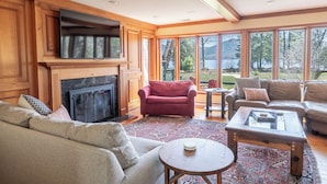 A spacious living room with a fireplace, multiple seating areas, and large windows offering a view of the outdoors. - Fish Point Landing (Diamond Point)
