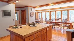 A spacious kitchen with wooden cabinetry, a large island, and a dining area with wooden chairs and a table. - Fish Point Landing (Diamond Point)