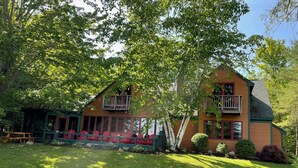A two-story wooden house with a balcony, a covered porch with red chairs, and a well-maintained lawn. - Fish Point Landing (Diamond Point)