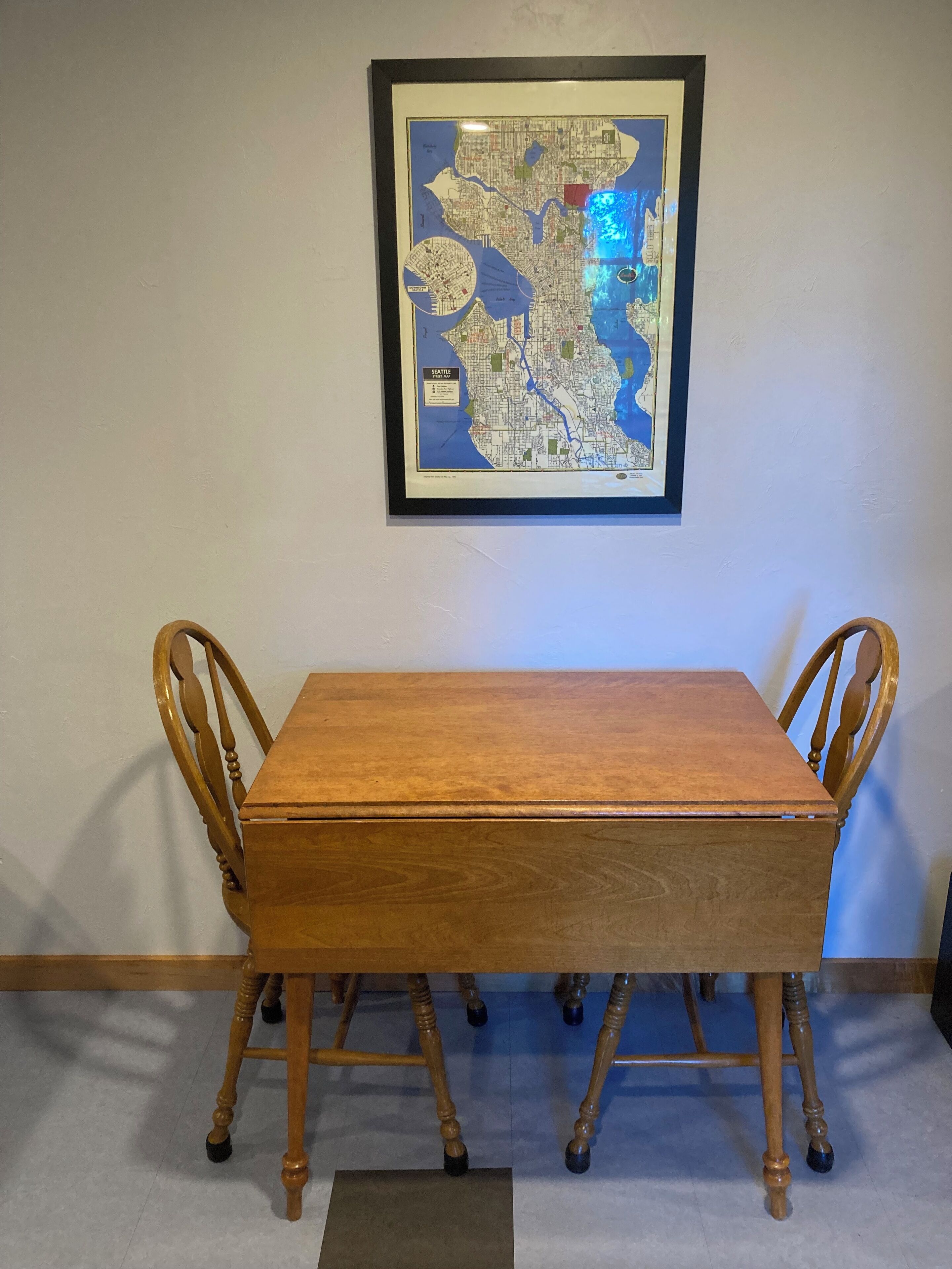 A framed map of Seattle on a wall, a wooden dining table with four chairs, and a small rug on the floor.