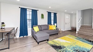 A modern living room with a grey sectional sofa, blue curtains, a wooden dining table with chairs, and a colorful rug. - Overland Park 4BR Home 2 Kings Garage Dog Friendly (Overland Park)