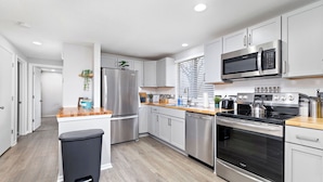 A modern kitchen with stainless steel appliances, white cabinetry, and a wooden countertop. - Overland Park 4BR Home 2 Kings Garage Dog Friendly (Overland Park)