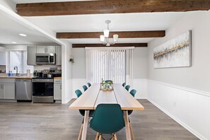 A modern kitchen with stainless steel appliances, a wooden dining table with chairs, and a chandelier. - Abstract Livin Free WiFi & Parking (Overland Park)