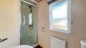 A bathroom with a glass shower enclosure, a white bathtub, a window with frosted glass, and a white radiator.