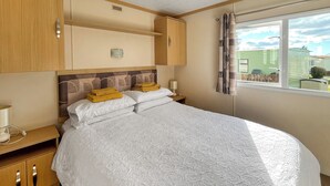 A neatly arranged bedroom with a large bed, a bedside table with a lamp, and a window with curtains.