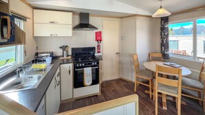 A compact kitchen with a stove, sink, and cabinets, a dining area with a table and chairs, and a window with a view.