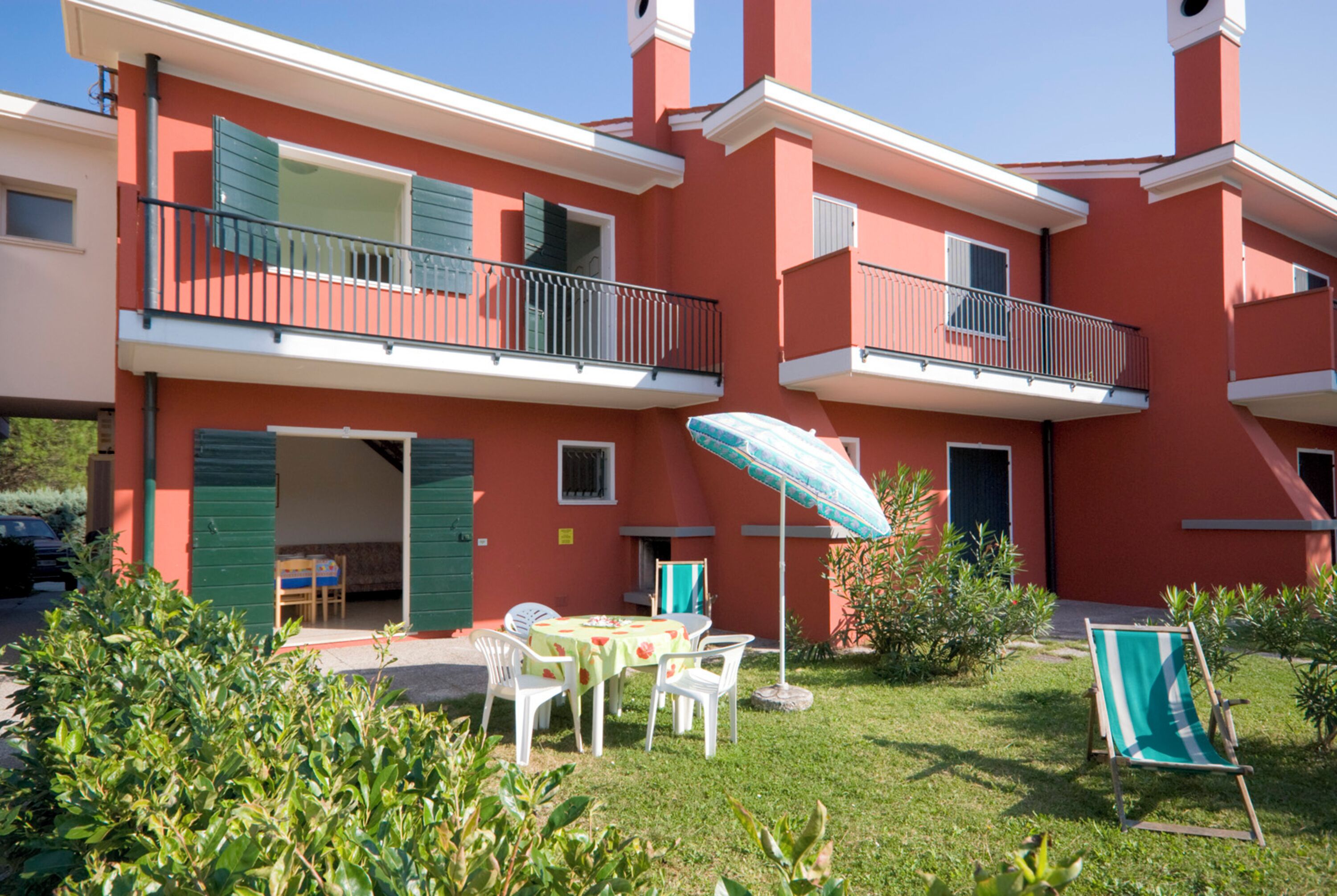 A two-story building with balconies, a patio area with a table and chairs, and a garden.
