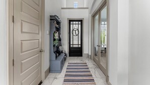 A hallway with a black door, a shoe rack, and a striped rug. - Luxury Retreat w/ Pool & Spa (Katy)