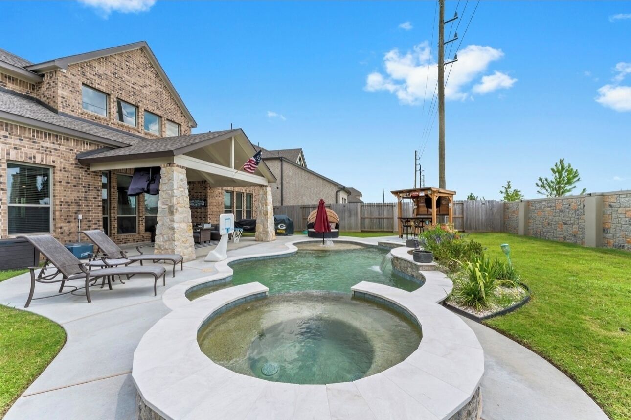 A backyard with a hot tub, a covered patio, and a brick house.