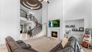 A spacious living room with a large sectional sofa, a fireplace, a TV mounted on the wall, and a staircase leading to an upper level. - Luxury Retreat w/ Pool & Spa (Katy)