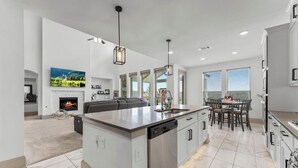 A modern kitchen with a central island, built-in dishwasher, and a dining area with a table and chairs. - Luxury Retreat w/ Pool & Spa (Katy)