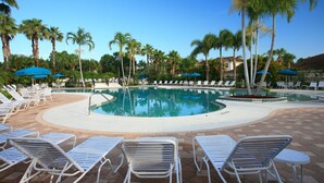 A pool area with lounge chairs and umbrellas, surrounded by palm trees. - Right Direction Rentals Studio Villa 8229 (Port St. Lucie)