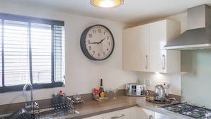 Una cocina con un reloj de pared, una estufa a gas, un tostador y un lavamanos con escurreplatos.
