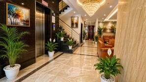 A hotel lobby with a marble floor, potted plants, a reception desk, a staircase, and a chandelier. - Hotel JMD - Managed by Kian (New Delhi)