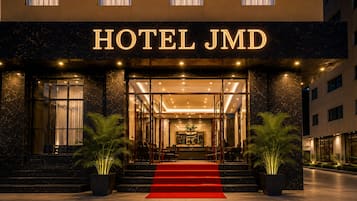 El exterior de un hotel con una entrada destacada, alfombra roja y plantas en macetas.