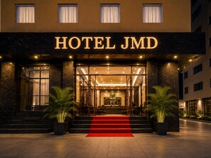 The exterior of a hotel with a prominent entrance, a red carpet, and potted plants. - Hotel JMD - Managed by Kian (New Delhi)