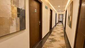 A hotel corridor with doors, a fire exit sign, and a hallway leading to a room. - Hotel JMD - Managed by Kian (New Delhi)
