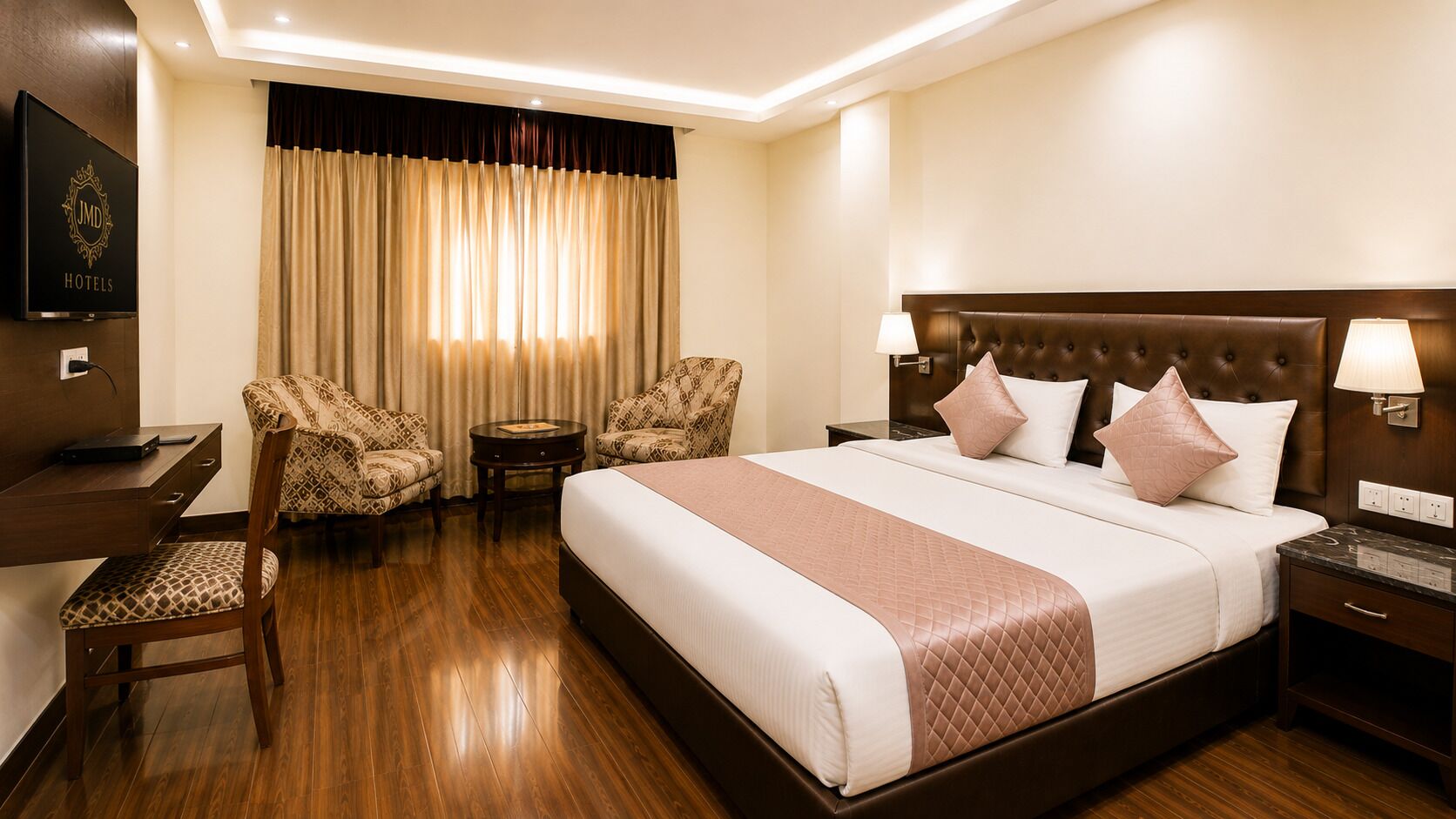 A hotel room with a large bed, two armchairs, a desk, and a TV.