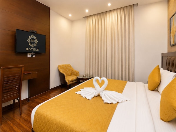 A hotel room with a bed, a desk, a chair, and a television displaying the hotel name.