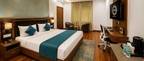 A hotel room with a bed, desk, chair, TV, and a minibar.
