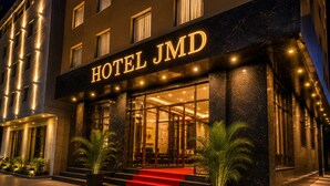 Een hotelingang met een bord waarop 'HOTEL JMD' staat, een rode loper en een trap naar de ingang.
