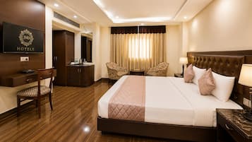 A hotel room with a large bed, a desk with a chair, a television, and a wardrobe.