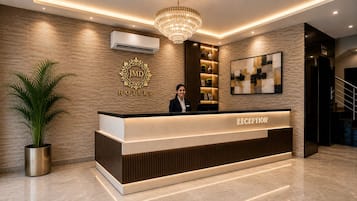 A hotel reception desk with a receptionist, a large chandelier, and a wall-mounted air conditioner.