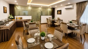 A dining area with multiple tables and chairs, a buffet setup, and a modern kitchen in the background. - Hotel JMD - Managed by Kian (New Delhi)