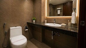 A modern bathroom with a toilet, sink, mirror, and shower. - Hotel JMD - Managed by Kian (New Delhi)