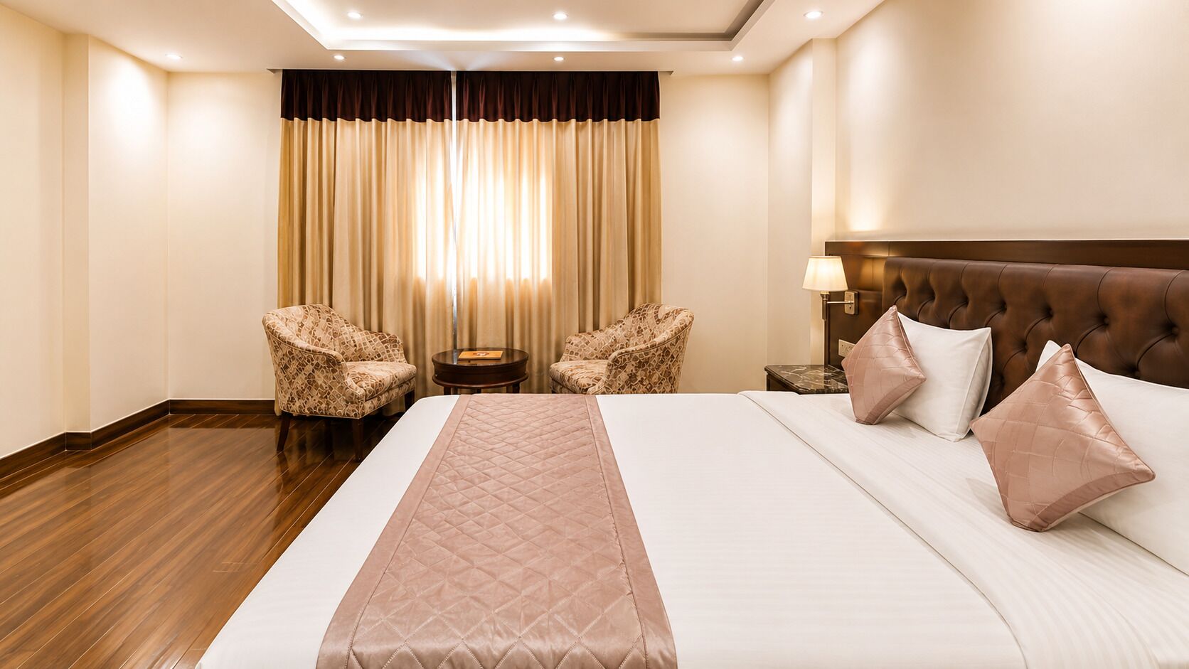 A hotel room with a large bed, two armchairs, a nightstand, and a headboard.