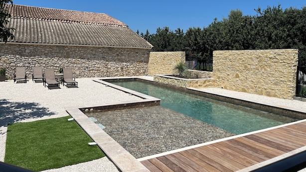 A swimming pool with a stone wall and a tiled roof structure. - Le Mas d'Archas (Allan)