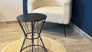 A corner room with a dark blue wall, a textured beige sofa, a black round table, and a woven rug. - Le Mas d'Archas (Allan)