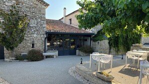 A stone building with a gravel courtyard, outdoor seating, and a covered patio area. - Le Mas d'Archas (Allan)