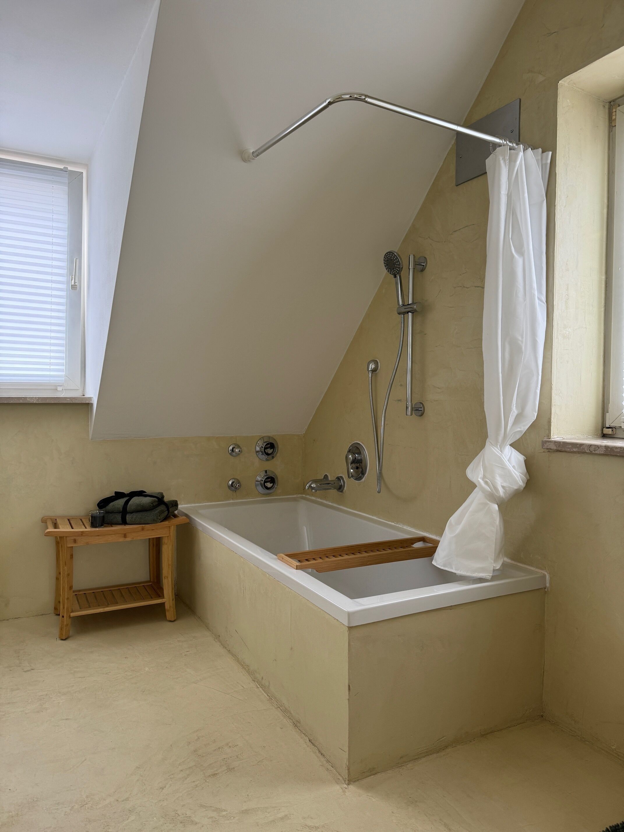 A modern bathroom with a freestanding bathtub, a wooden side table, and a shower area.