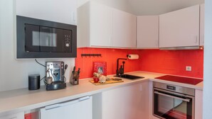 A modern kitchen with white cabinets, a black microwave, a red backsplash, and a built-in oven.