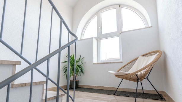 A staircase with metal railings, a wicker chair, a potted plant, and a window with a view of the sky.