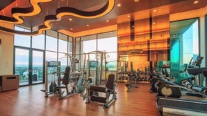 Ein modernes Fitnessstudio mit verschiedenen Trainingsgeräten, großen Fenstern und einer hohen Decke mit besonderer Beleuchtung.