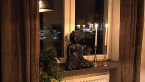 Une fenêtre avec une statue représentant une figure assise, un radiateur en dessous et une plante sur la gauche.