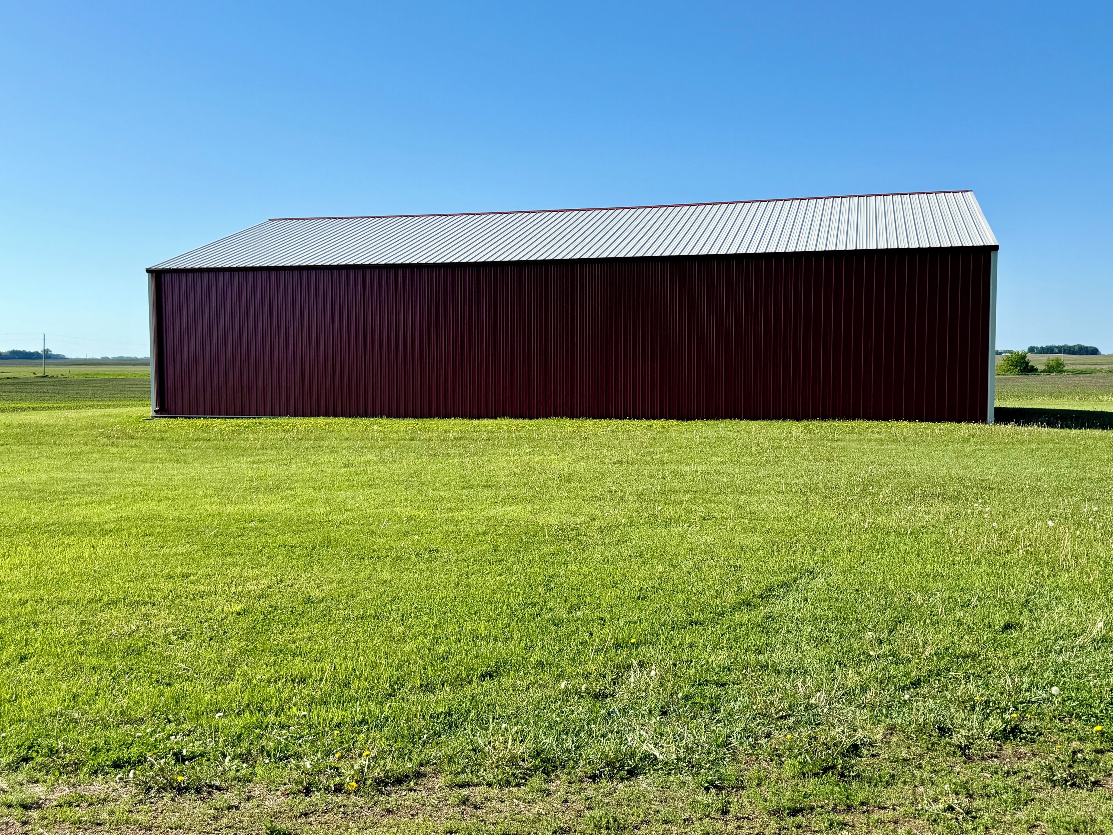 A large, single-story building with a dark exterior and a sloped roof, situated in a grassy field with a clear sky.
