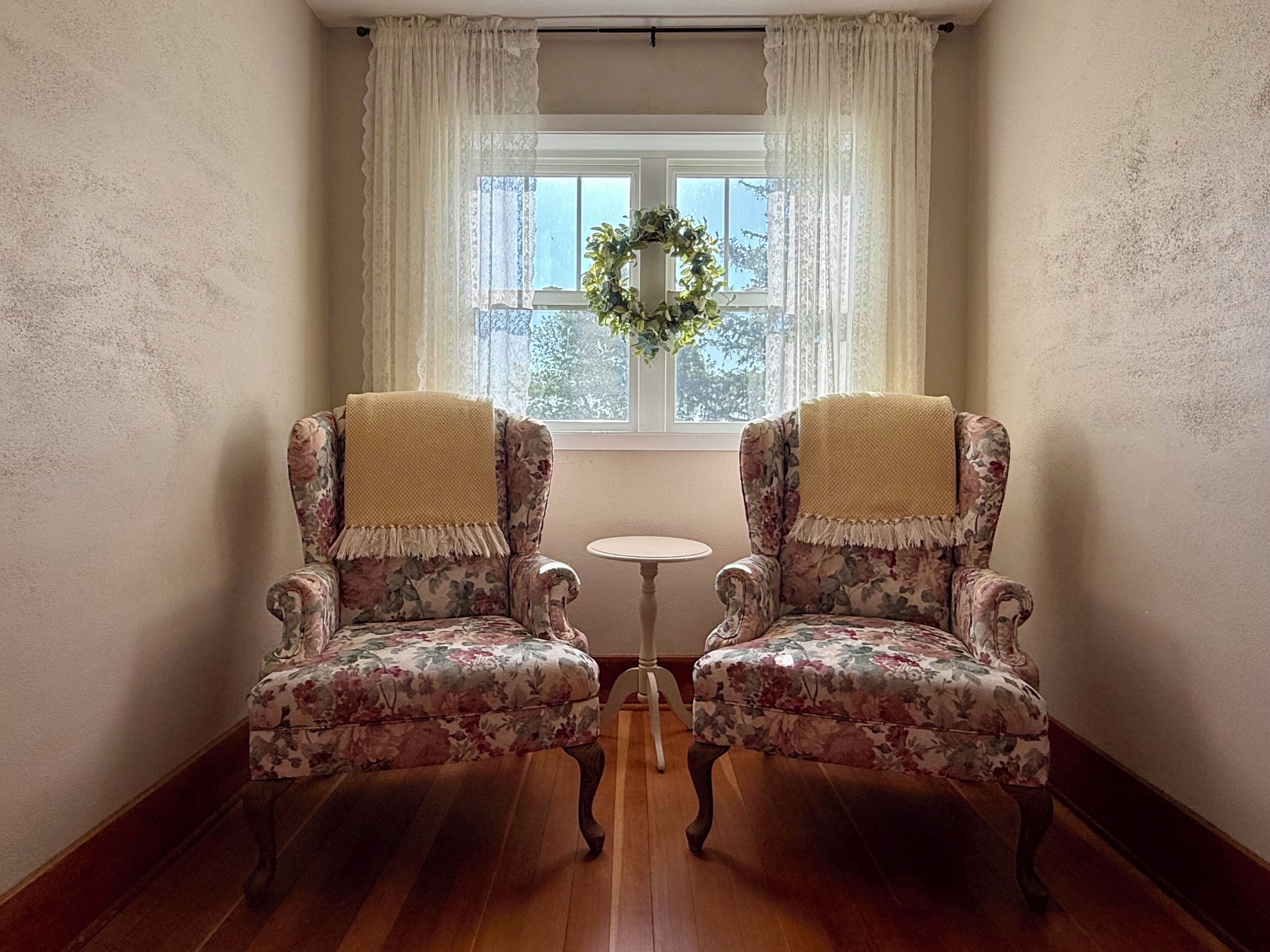 Two upholstered armchairs with floral upholstery and fringed edges, positioned facing each other with a small round table between them.