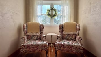 Two upholstered armchairs with floral upholstery and fringed edges, positioned facing each other with a small round table between them.