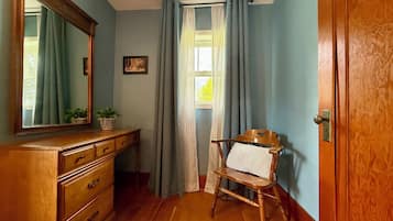 A room with a wooden dresser, a chair, a window with curtains, and a door.
