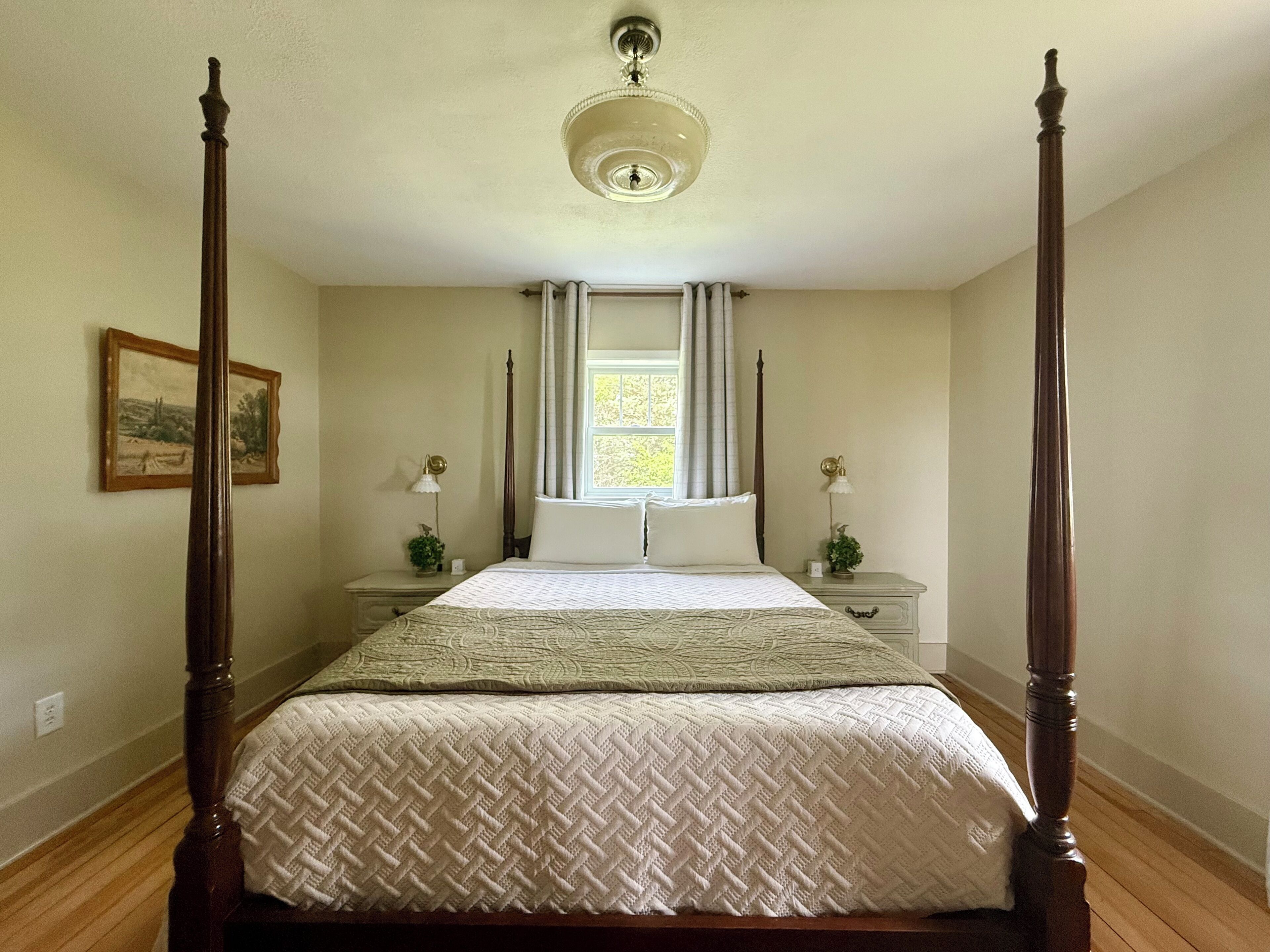 A four-poster bed with a canopy, a nightstand with a lamp, and a window with curtains.