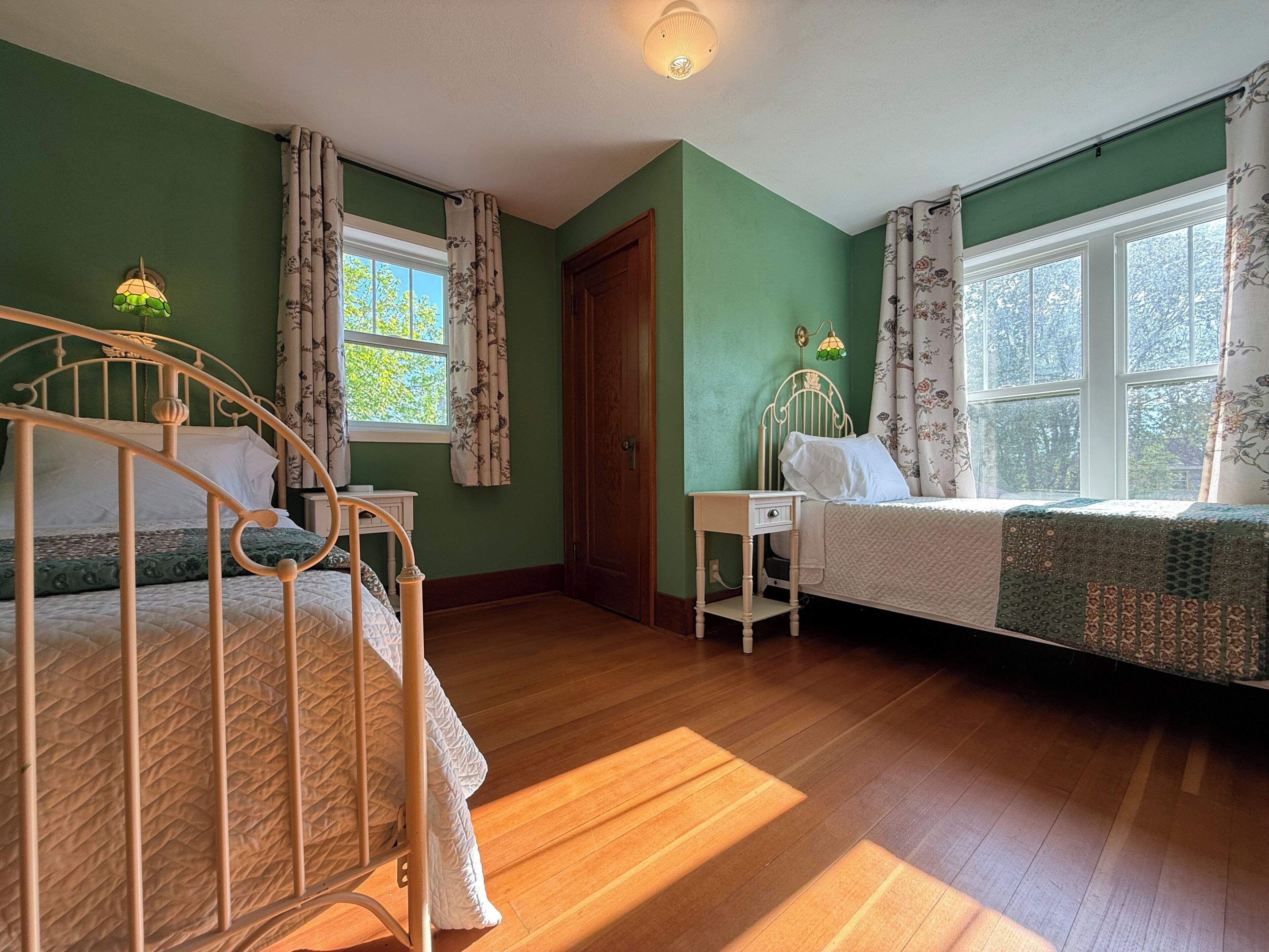 A room with two beds, a wooden floor, and a window with curtains.