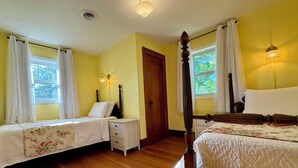 Ein Zimmer mit zwei Betten, einem Nachttisch, einer Holztür und einem Fenster mit Vorhängen.