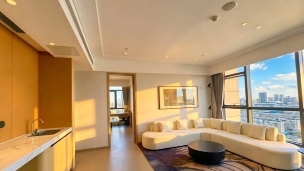 A modern living room with a large window, a sofa, and a kitchen area. - Yancheng Baolong Yiyue Select Hotel (Yancheng)