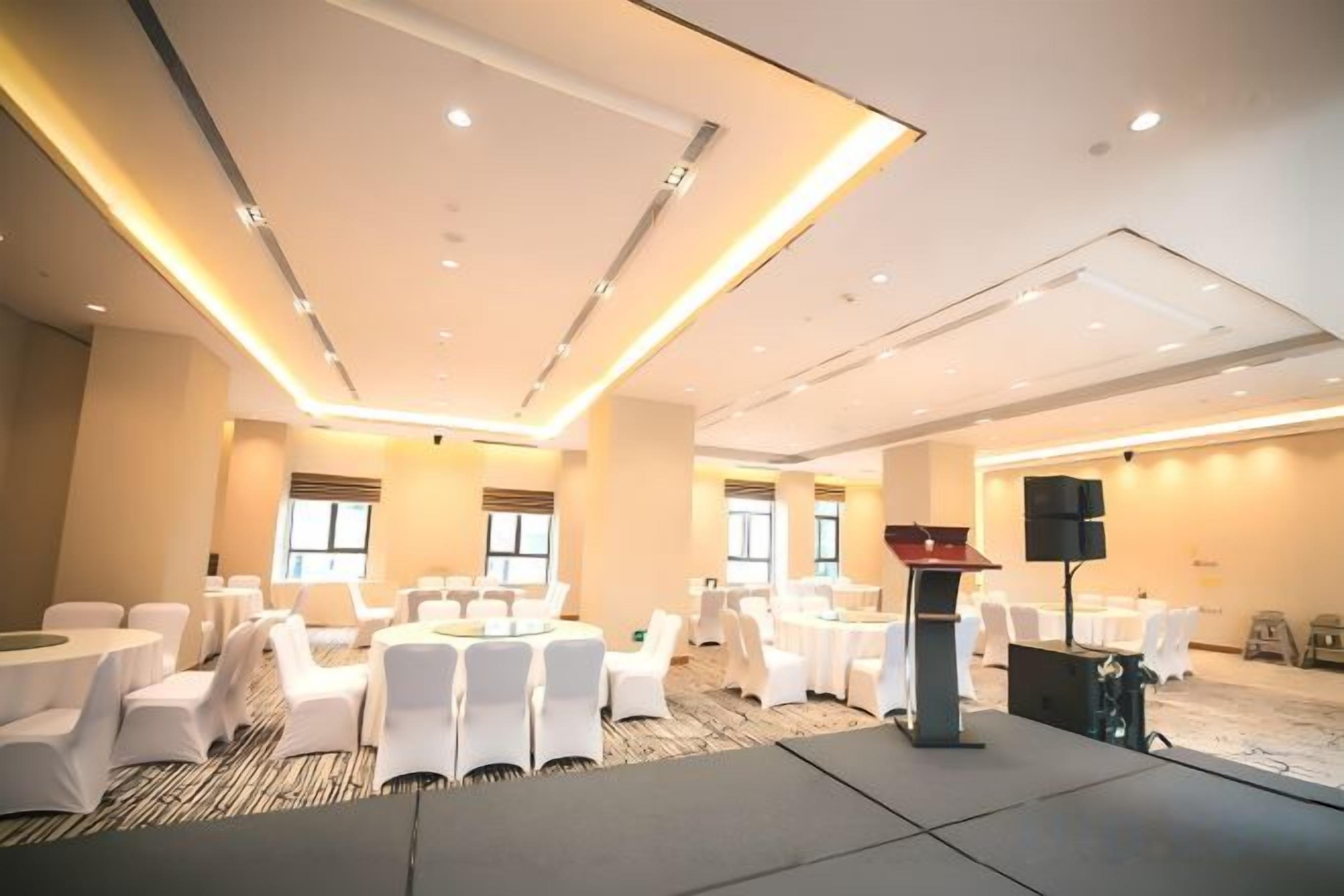 Un salón de conferencias con mesas redondas, sillas blancas, un atril y suelo alfombrado.