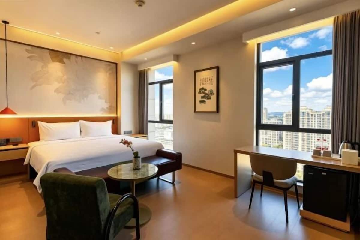 Une chambre dâhĂŽtel Ă©quipĂ©e dâun lit, dâun bureau, dâune chaise et dâune grande fenĂȘtre donnant sur la ville.