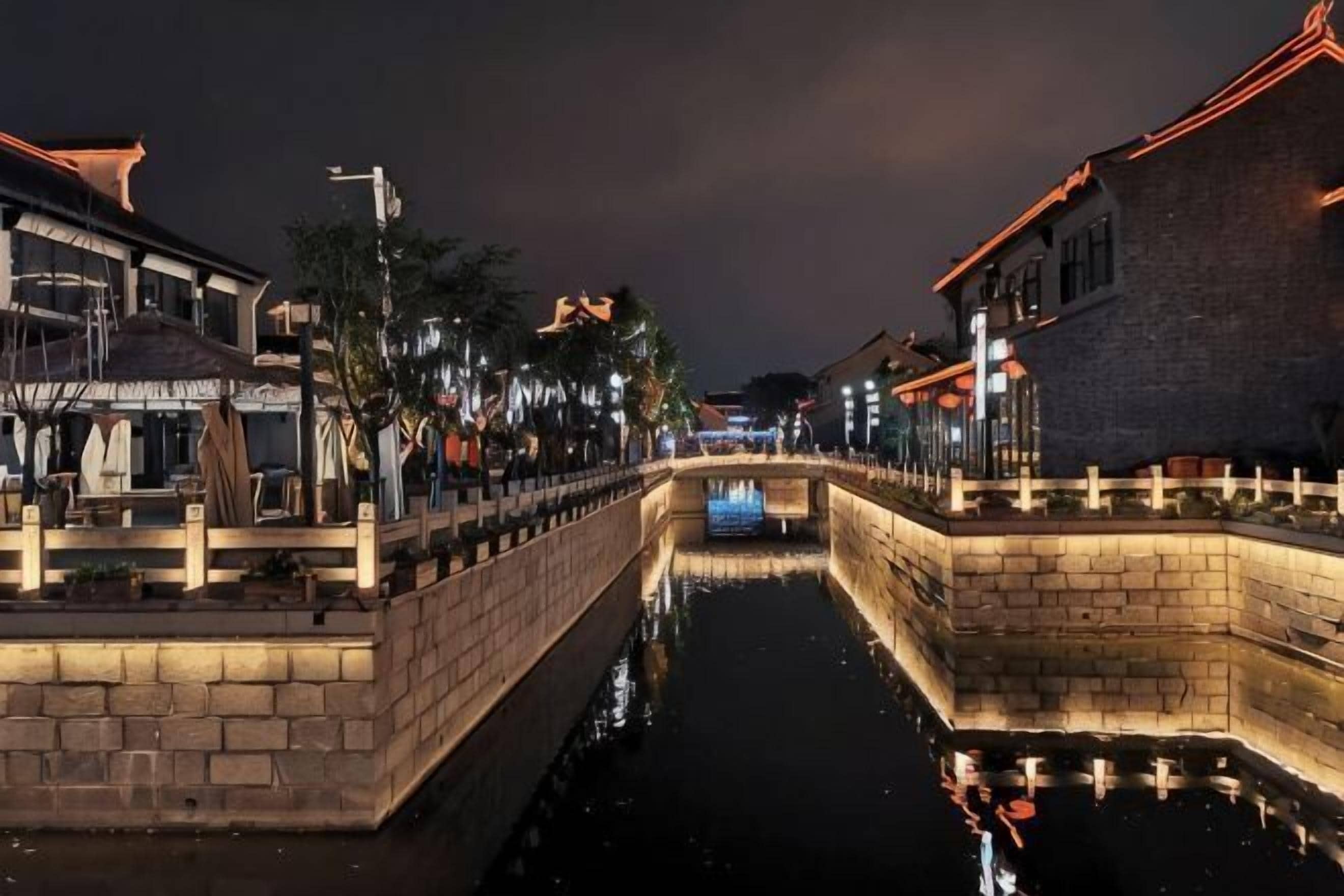 Ein Kanal mit Steinmauern und einer Brücke, gesäumt von Gebäuden mit traditioneller Architektur und Außenbereichen zum Verweilen.
