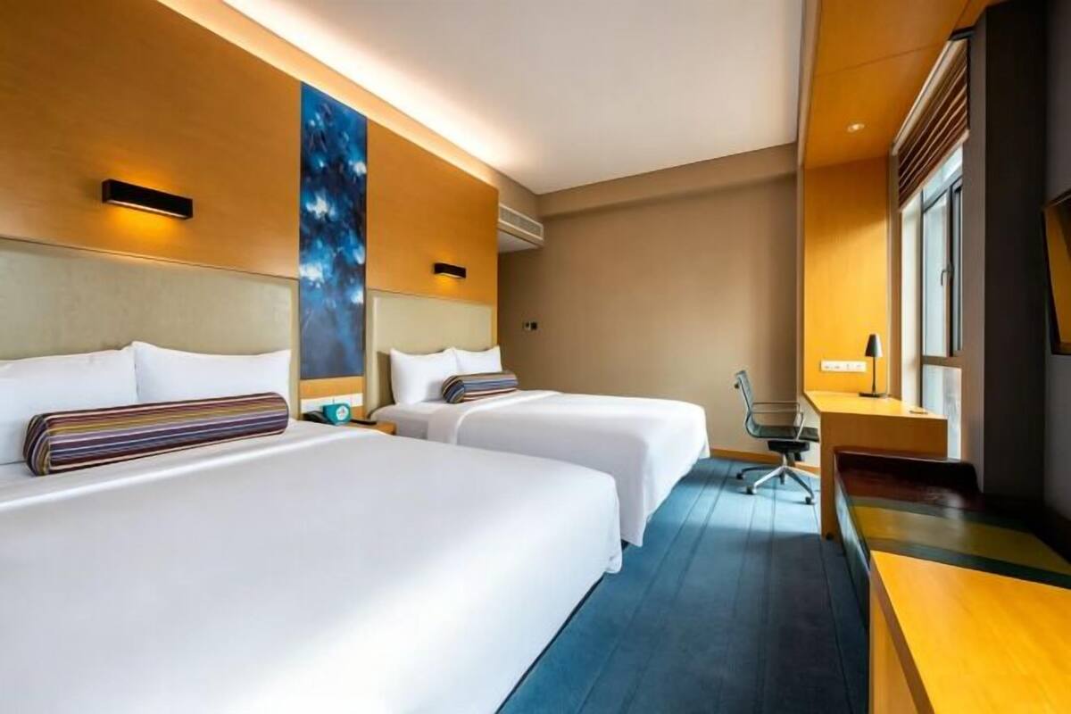 Hotellihuone, jossa on kaksi sänkyä, työpöytä, tuoli ja suuri ikkuna.